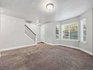Unfurnished living room with carpet, stairs, and a textured ceiling