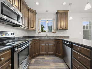 Kitchen with appliances with stainless steel finishes, recessed lighting, dark stone countertops, dark wood-style flooring, and decorative light fixtures