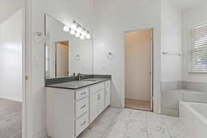 Full bath with vanity, a bath, and light marble finish floors