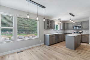 Kitchen featuring gray cabinets, glass insert cabinets, a center island, decorative backsplash, and appliances with stainless steel finishes