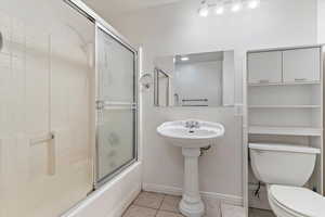 Full bathroom with light tile patterned floors and bath / shower combo with glass door