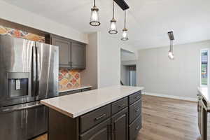 Kitchen featuring stainless steel fridge, decorative light fixtures, tasteful backsplash, a kitchen island, and light wood-style flooring