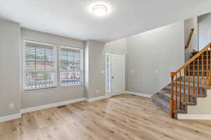 Foyer entrance with stairs, light wood-type flooring, and a textured ceiling