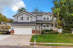 View of front of property with a front yard, covered porch, brick siding, driveway, and a garage
