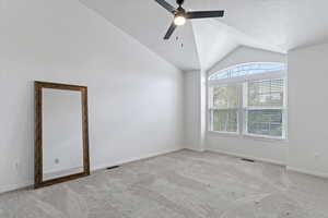 Empty room featuring vaulted ceiling, carpet, a ceiling fan, and a textured ceiling