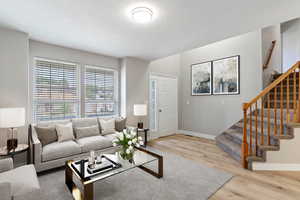 Virtually staged. Living room with light wood-style floors, a textured ceiling, and stairway