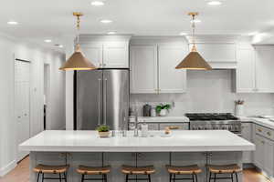 Kitchen with gray cabinetry, decorative backsplash, light wood-style floors, a kitchen breakfast bar, and recessed lighting