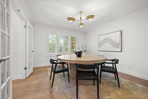 Dining area featuring ornamental molding, light wood-style flooring, a chandelier, and french doors