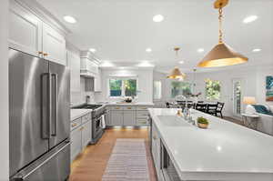 Kitchen with high end appliances, light wood-style flooring, hanging light fixtures, recessed lighting, and light stone counters