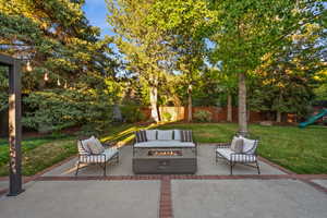 Fenced backyard with a patio, an outdoor living space with a fire pit, a playground, and view of wooded area