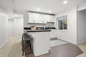 Kitchen with ornamental molding, white cabinets, a kitchen bar, recessed lighting, and dark colored carpet