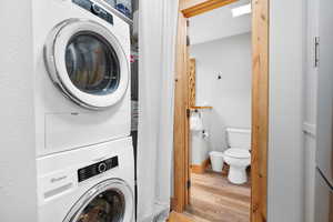 Laundry room featuring wood finished floors, stacked washing machine and dryer, and a textured wall