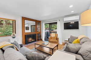 Living area with wood finished floors, a fireplace with flush hearth, a wall unit AC, recessed lighting, and a wall mounted AC