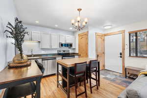 Kitchen featuring appliances with stainless steel finishes, hanging light fixtures, white cabinetry, a chandelier, and light wood-type flooring