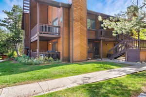 Back of house with a chimney, a balcony, a yard, and stairway