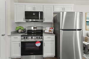 Kitchen with stainless steel appliances, backsplash, white cabinets, and light stone counters