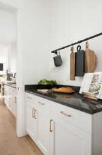 Bar area featuring white cabinetry, light wood-style floors, and dark stone countertops