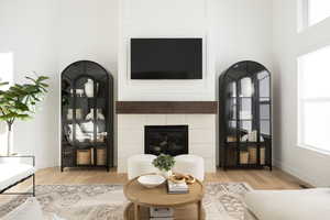 Living area featuring a tiled fireplace, light wood finished floors, and a high ceiling