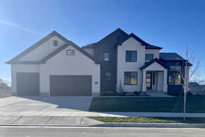 Modern inspired farmhouse featuring a garage, driveway, brick siding, board and batten siding, and a front yard