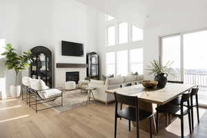 Dining area with light wood-type flooring, a glass covered fireplace, and a towering ceiling