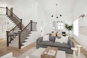 Living room featuring high vaulted ceiling, light wood-style floors, and stairway