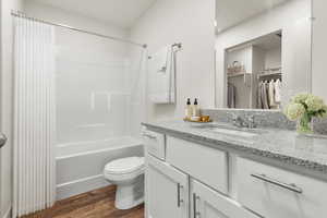 Full bath with shower / bathtub combination with curtain, vanity, dark wood-style flooring, and a walk in closet