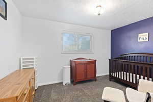 Bedroom with a nursery area, dark colored carpet, and a textured ceiling