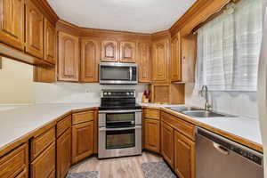 Kitchen with appliances with stainless steel finishes, light countertops, brown cabinets, light wood-style floors, and a textured ceiling