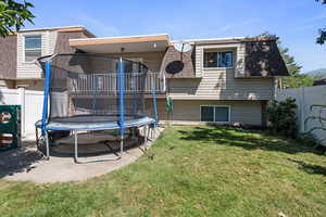 Rear view of house with a fenced backyard, mansard roof, a trampoline, and roof with shingles