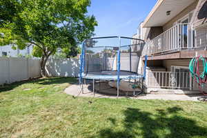 Fenced backyard featuring a trampoline, a balcony, and a patio