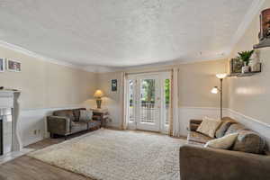Living room with crown molding, light wood-type flooring, a textured ceiling, and a tile fireplace