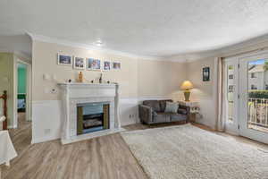 Living area with light wood finished floors, a textured ceiling, crown molding, a tile fireplace, and a wainscoted wall