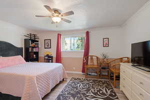Bedroom featuring light wood finished floors, crown molding, a textured ceiling, and ceiling fan