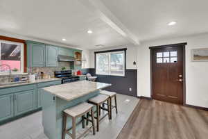 Kitchen with light wood-style flooring, a wainscoted wall, a center island, a kitchen breakfast bar, and light stone counters