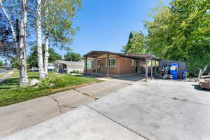 View of front facade featuring brick siding, concrete driveway, a carport, a front lawn, and a patio