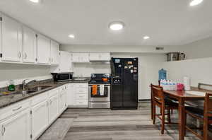 Basement kitchen featuring appliances with stainless steel finishes, dark stone counters, white cabinetry, light wood-style flooring, and recessed lighting