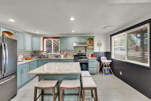 Kitchen featuring open shelves, appliances with stainless steel finishes, a kitchen island, a breakfast bar, and recessed lighting