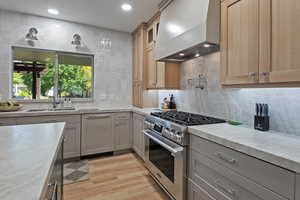 Kitchen featuring high end stove, premium range hood, glass insert cabinets, tasteful backsplash, and gray cabinetry