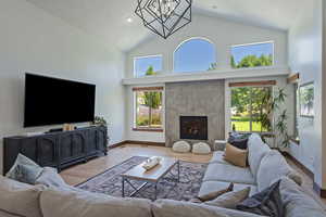 Living room with high vaulted ceiling, a premium fireplace, wood finished floors, and a chandelier