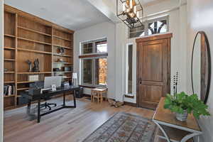Office area with light wood finished floors, a chandelier, and built in shelves