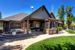 Rear view of property with a covered hot tub, exterior kitchen, a wooden deck, stucco siding, and a pergola