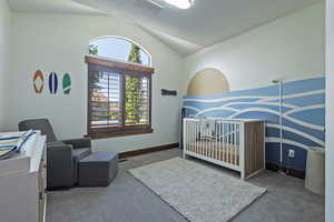Bedroom featuring a nursery area, lofted ceiling, and carpet
