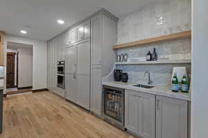 Indoor wet bar featuring gray cabinets, backsplash, open shelves, wine cooler, and light wood-style flooring