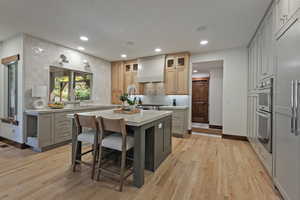 Kitchen featuring a kitchen bar, gray cabinetry, backsplash, a center island, and light wood-style flooring