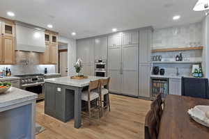Kitchen featuring backsplash, gray cabinets, wine cooler, premium range hood, and premium appliances