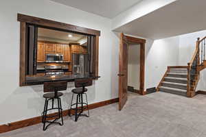 Kitchen featuring a kitchen breakfast bar, appliances with stainless steel finishes, brown cabinetry, light carpet, and recessed lighting