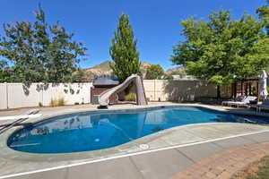View of pool featuring a water slide, a fenced backyard, a mountain view, and a patio area