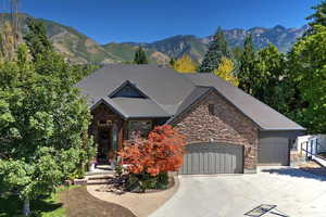 View of front of property with driveway, an attached garage, stone siding, and a mountain view