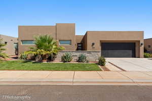 Pueblo revival-style home featuring stucco siding, driveway, an attached garage, and a front yard