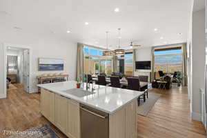 Kitchen with open floor plan, dishwasher, light wood-style floors, recessed lighting, and a center island with sink